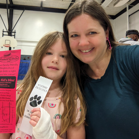 Therese and her daughter smile at the camera while her daughter holds up awards.
